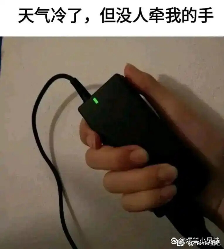 A hand holds a small black device with a lit green light that is connected to a black wire, with the caption "It's cold, but nobody held my hand" at the top. (Captioned by AI)