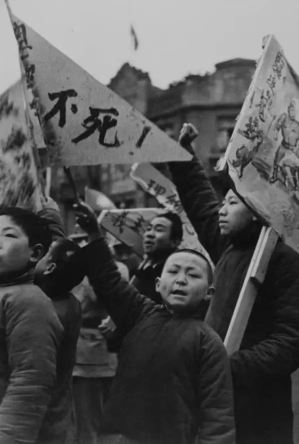 The black and white photo shows a group of young protestors, their arms raised and holding flags with Chinese characters. (Captioned by AI)