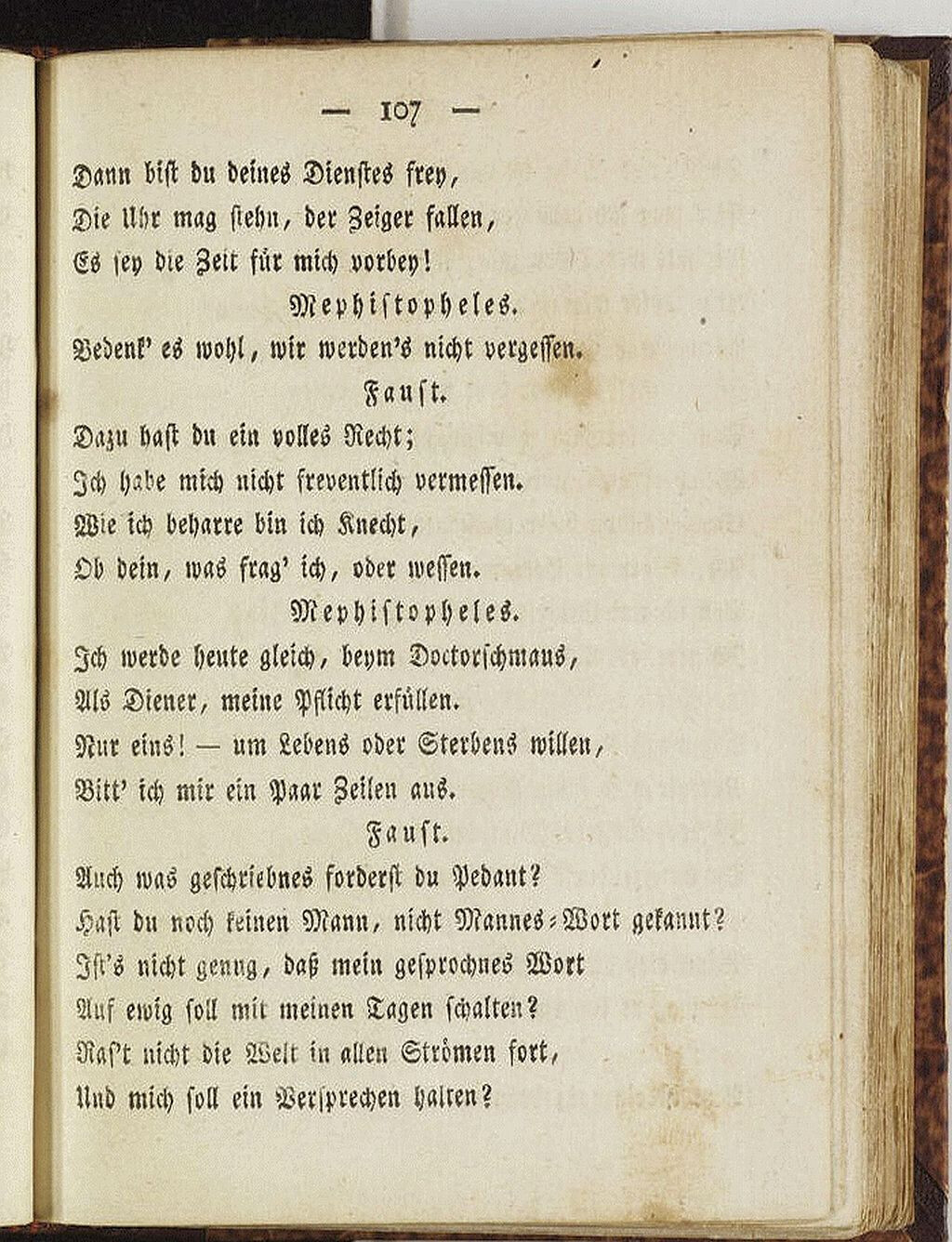 The image shows an opened book with a page displaying a portion of a play written in the German language, possibly a historical or classical piece, with character names like Faust and Mephistopheles indicated. (Captioned by AI)