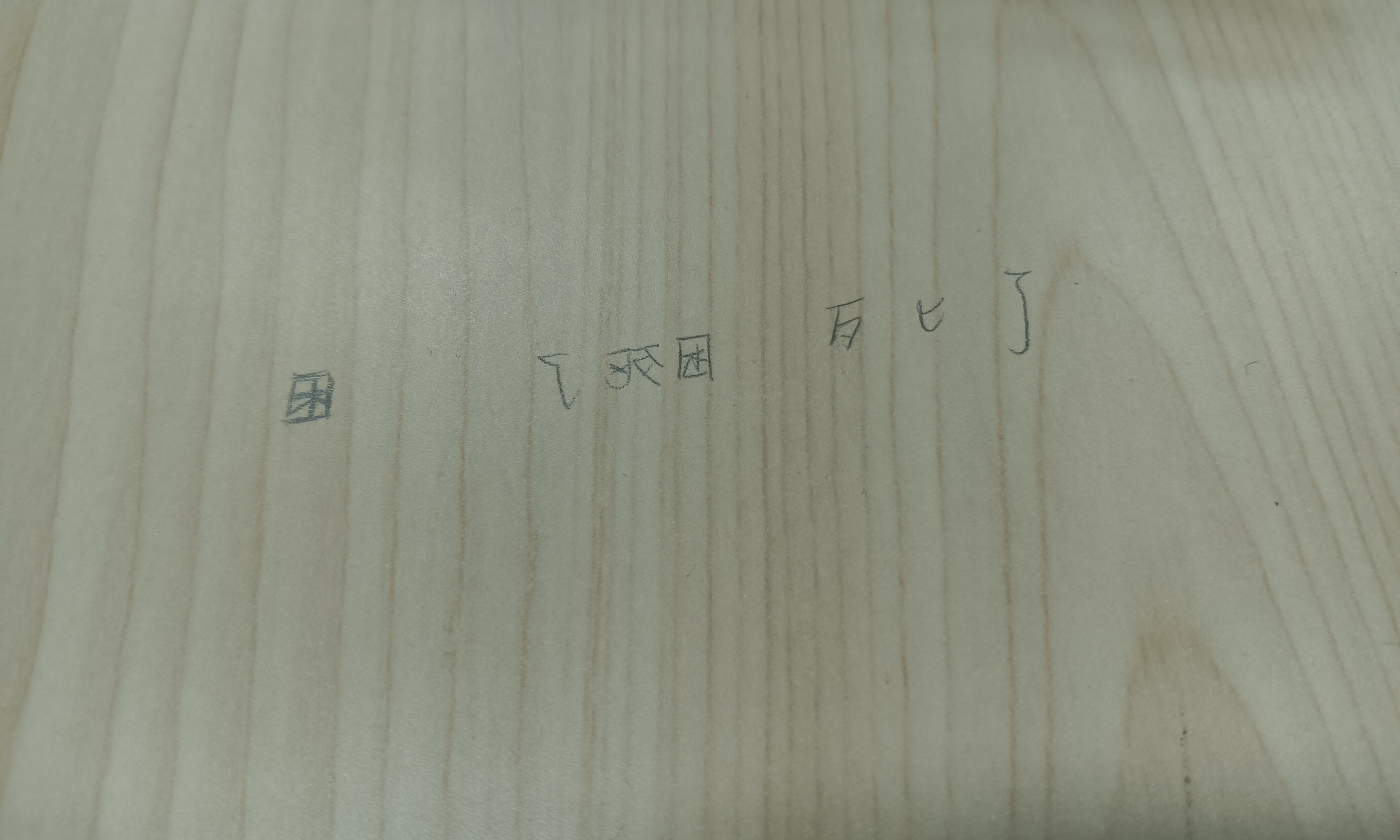 A light-colored wooden surface has the Japanese characters for "I returned home" written on it in pencil. (Captioned by AI)