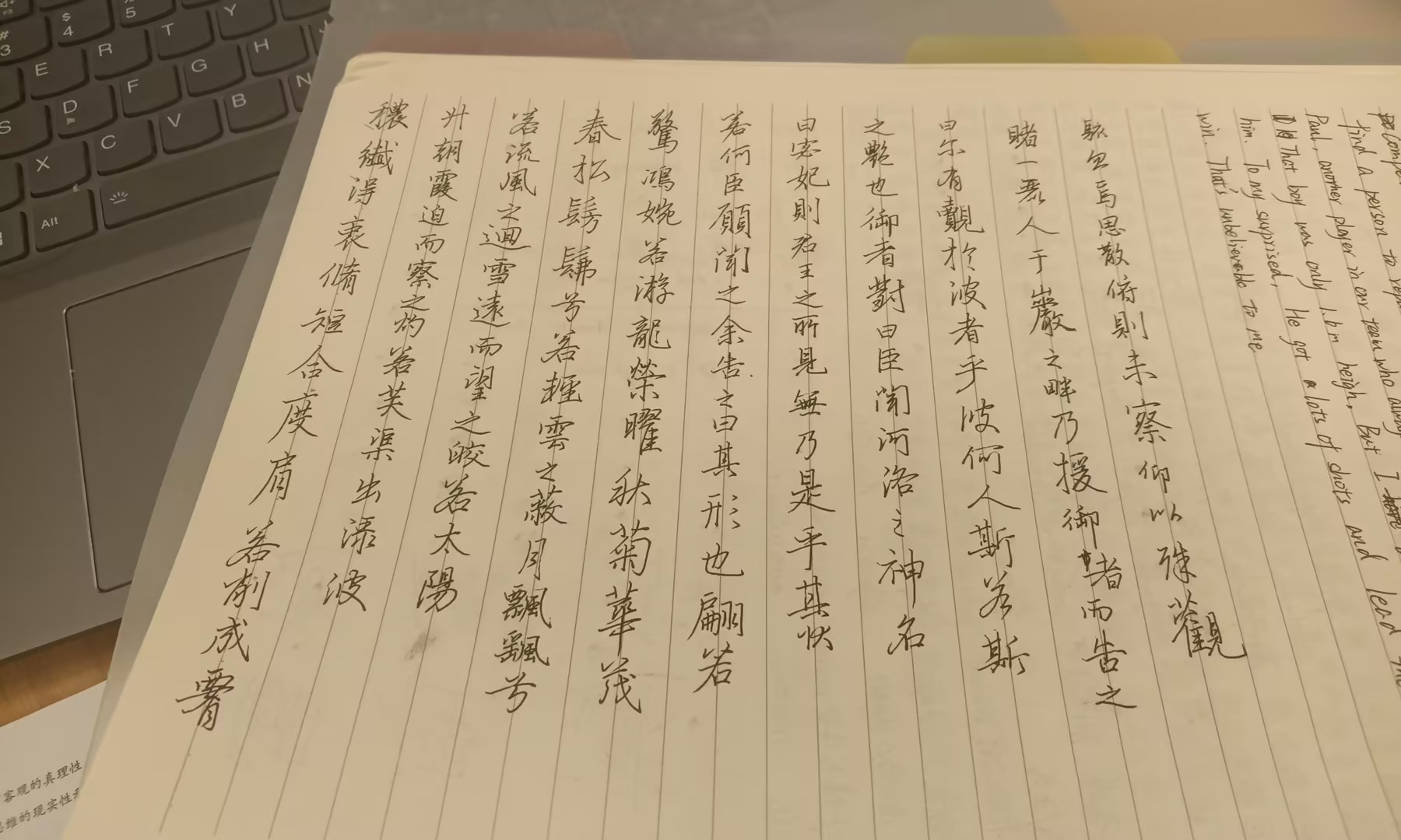 A notebook filled with Chinese characters lies open next to the corner of a laptop keyboard. (Captioned by AI)