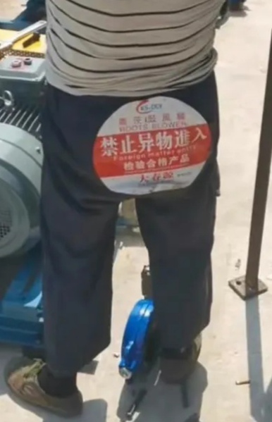 A person wearing dark blue pants with a red and white circular advertisement on the back is standing near some machinery. (Captioned by AI)