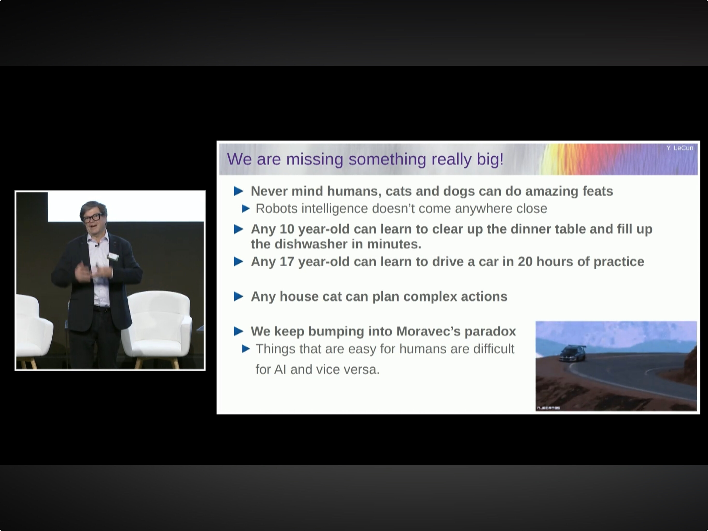 A man on stage is giving a presentation about Moravec's paradox, a concept which states that tasks easy for humans are hard for artificial intelligence and vice versa. (Captioned by AI)